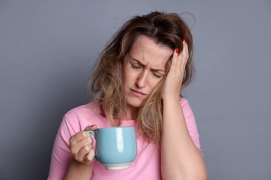 Photo of Woman with cup of coffee suffering from hangover on grey background