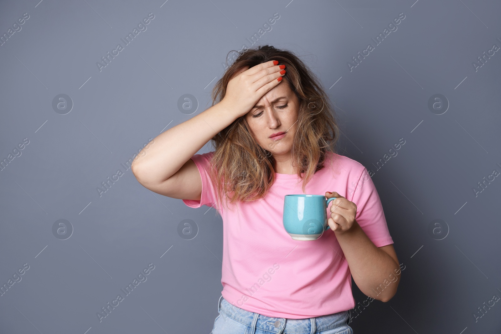 Photo of Woman with cup of coffee suffering from hangover on grey background