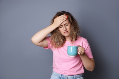 Photo of Woman with cup of coffee suffering from hangover on grey background