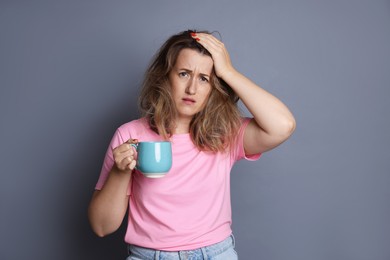 Photo of Woman with cup of coffee suffering from hangover on grey background
