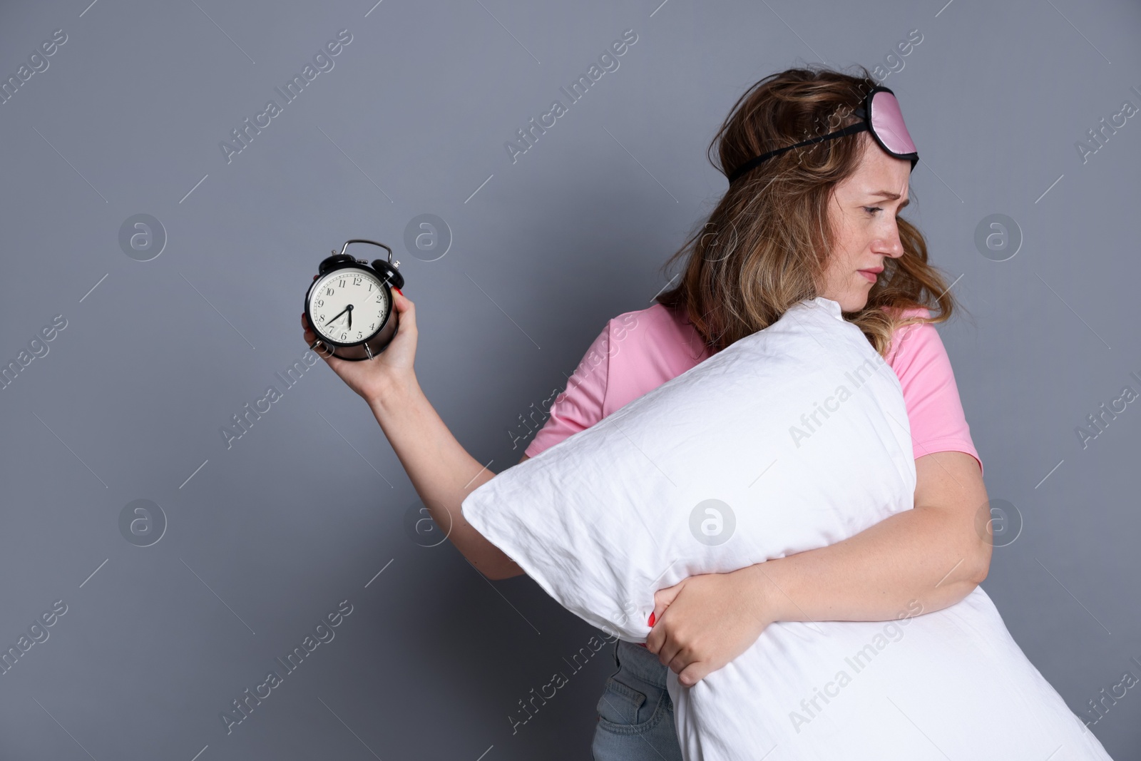 Photo of Woman with pillow and alarm clock suffering from hangover on grey background