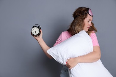 Photo of Woman with pillow and alarm clock suffering from hangover on grey background