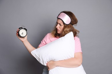 Photo of Woman with pillow and alarm clock suffering from hangover on grey background