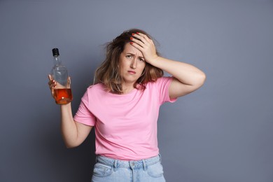 Photo of Woman with bottle of alcoholic drink suffering from hangover on grey background