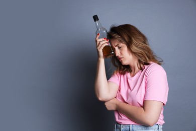 Photo of Woman with bottle of alcoholic drink suffering from hangover on grey background. Space for text
