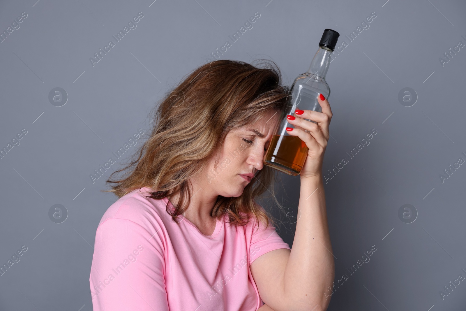 Photo of Woman with bottle of alcoholic drink suffering from hangover on grey background