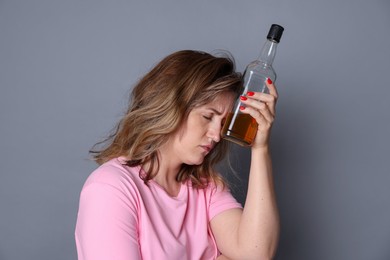 Photo of Woman with bottle of alcoholic drink suffering from hangover on grey background