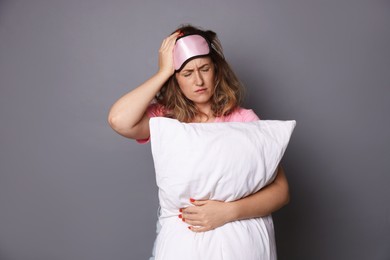 Photo of Woman with pillow suffering from hangover on grey background