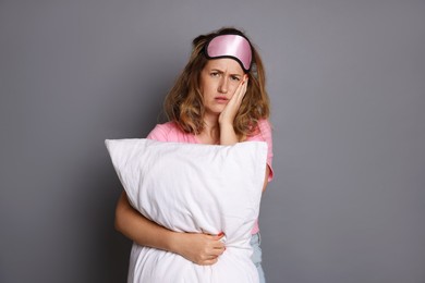 Photo of Woman with pillow suffering from hangover on grey background