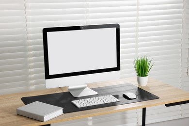 Photo of Stylish workplace with computer and black mousepad on wooden table indoors. Space for text