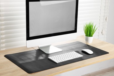 Photo of Stylish workplace with computer and black mousepad on wooden table indoors, closeup. Space for text