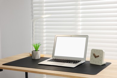 Photo of Stylish workplace with laptop and black mousepad on wooden table indoors. Space for text
