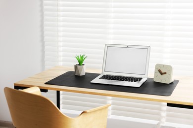 Photo of Stylish workplace with laptop and black mousepad on wooden table indoors. Space for text