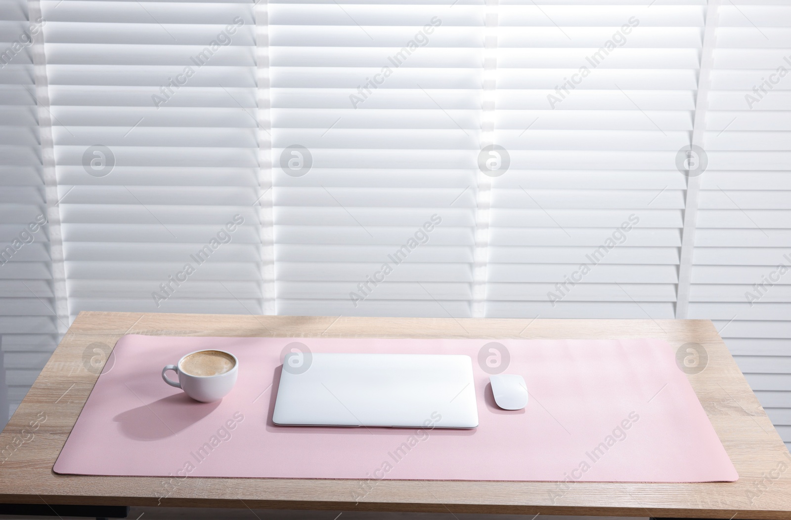 Photo of Stylish workplace with laptop and pink mousepad on wooden table indoors. Space for text
