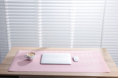 Photo of Stylish workplace with laptop and pink mousepad on wooden table indoors. Space for text