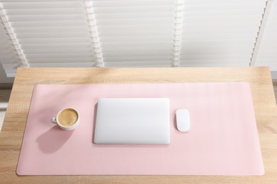 Photo of Stylish workplace with laptop and pink mousepad on wooden table indoors, above view