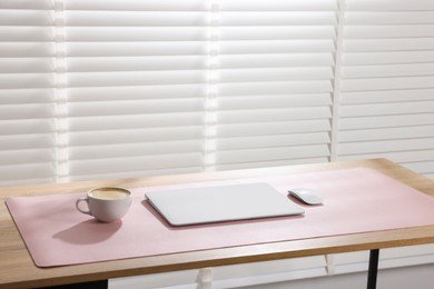 Photo of Stylish workplace with laptop and pink mousepad on wooden table indoors. Space for text