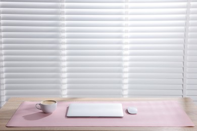 Photo of Stylish workplace with laptop and pink mousepad on wooden table indoors. Space for text