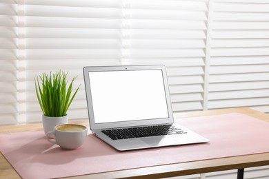 Photo of Stylish workplace with laptop and pink mousepad on wooden table indoors. Space for text