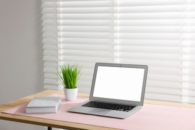 Photo of Stylish workplace with laptop and pink mousepad on wooden table indoors. Space for text