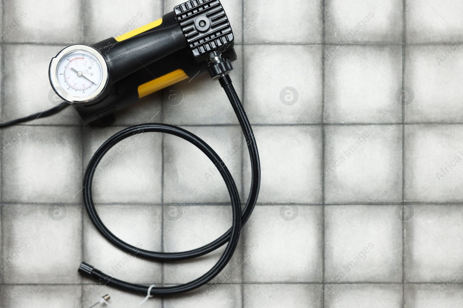 One tire inflation gun with gauge on light tiled background, top view. Space for text Photo of One tire inflation gun with gauge on light tiled background, top view. Space for text