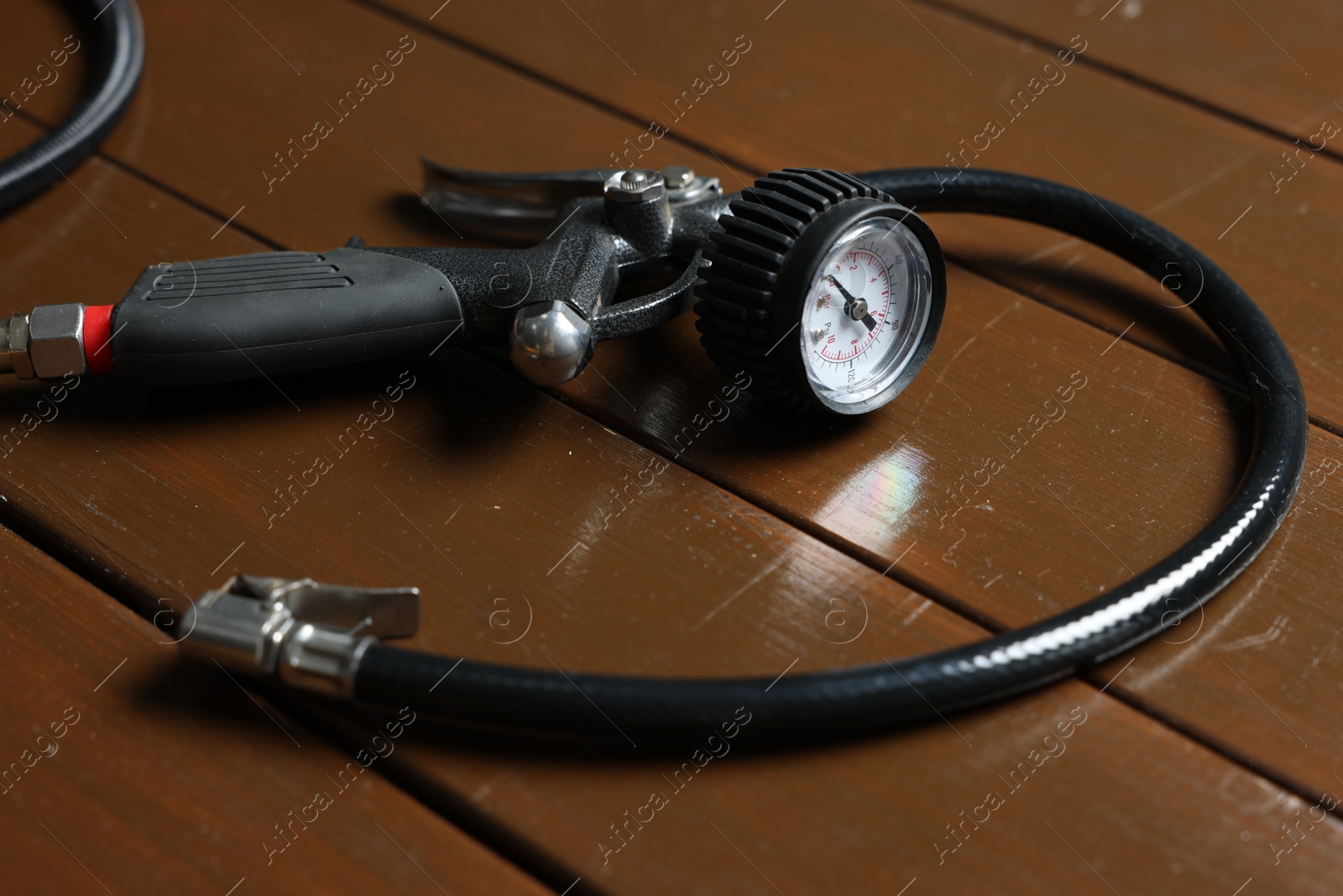 Photo of One tire inflation gun with gauge on wooden background, closeup