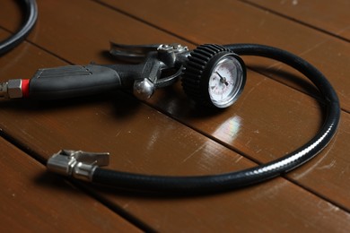 Photo of One tire inflation gun with gauge on wooden background, closeup