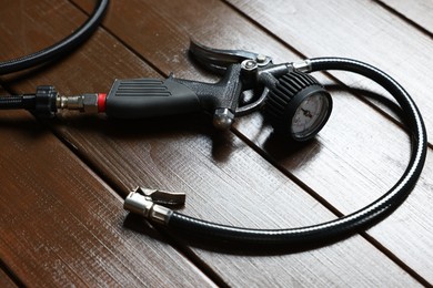 Photo of One tire inflation gun with gauge on wooden background, closeup