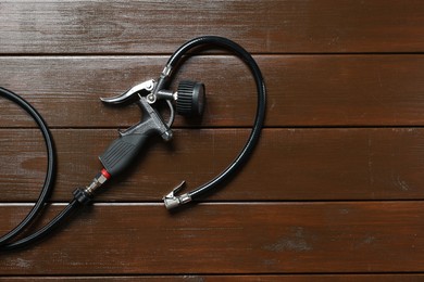 Photo of One tire inflation gun with gauge on wooden background, top view