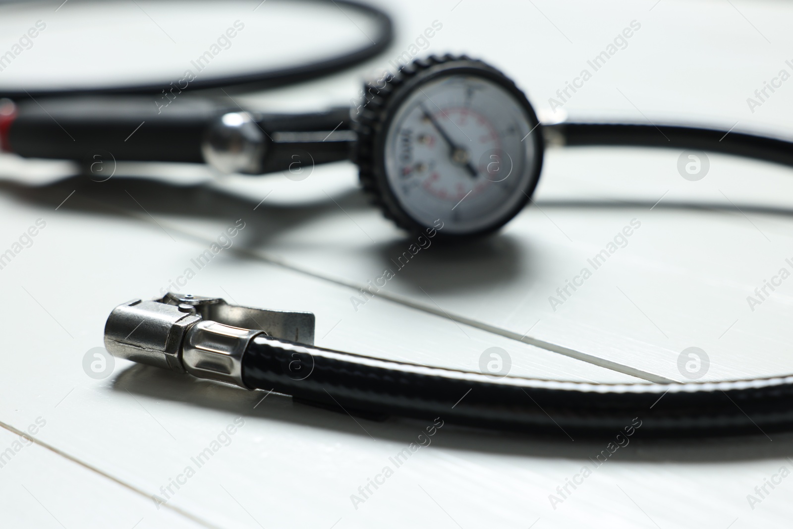 Photo of One tire inflation gun with gauge on white wooden background, closeup