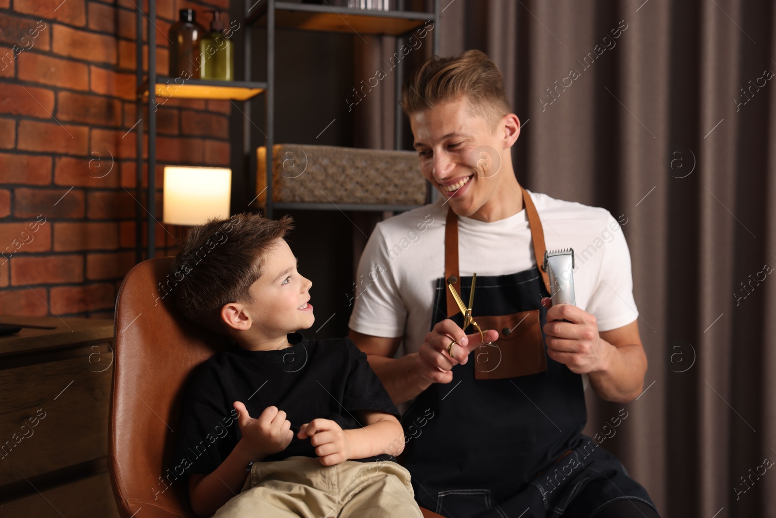 Professional barber with scissors, trimmer and little boy in barbershop Photo of Professional barber with scissors, trimmer and little boy in barbershop