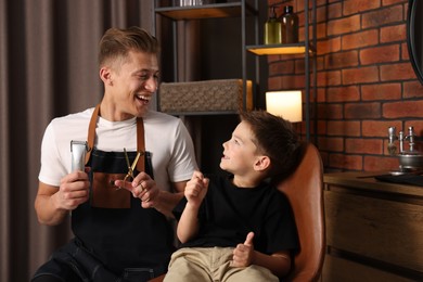 Photo of Professional barber with scissors, trimmer and little boy in barbershop