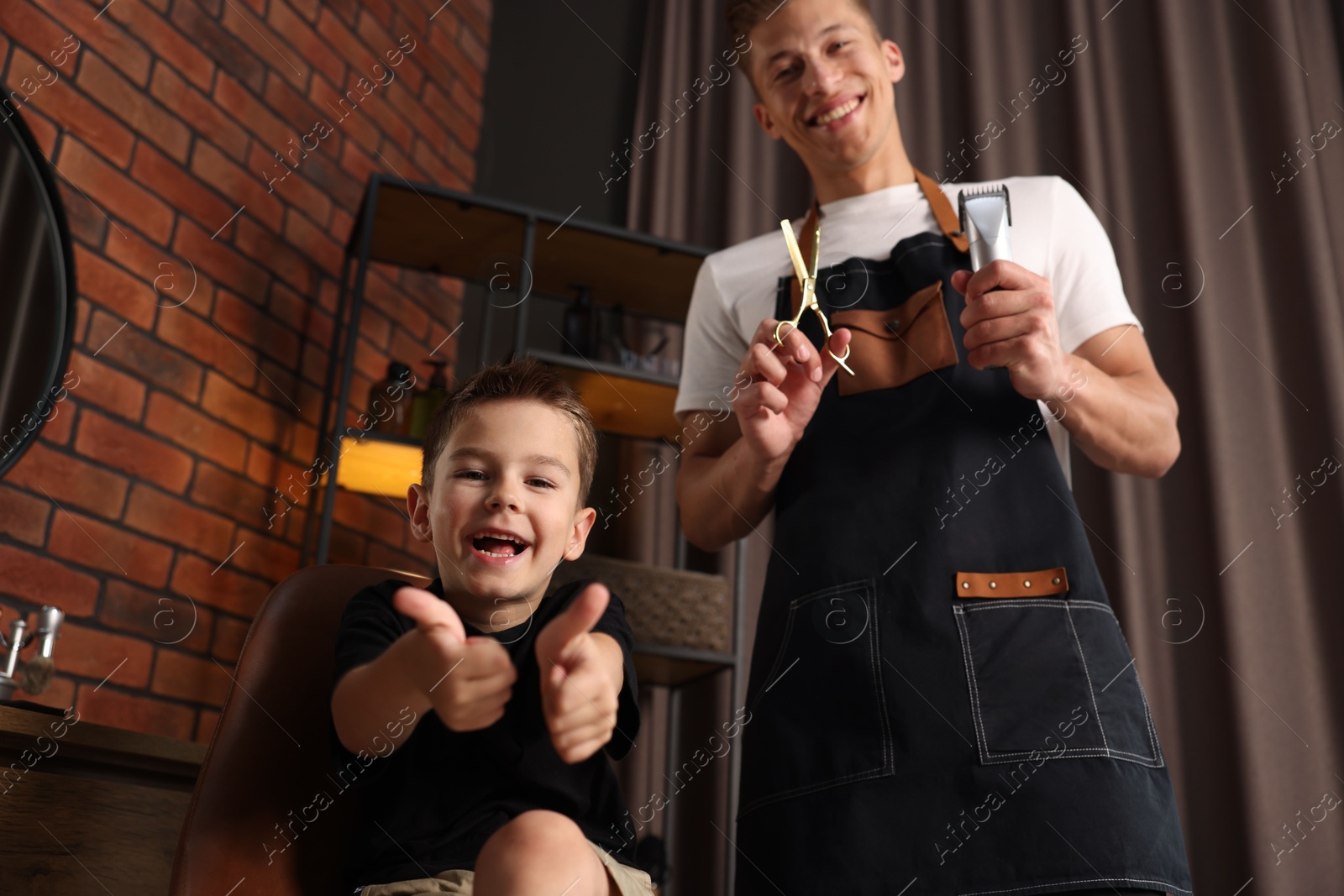 Professional barber with scissors, trimmer and little boy in barbershop, low angle view Photo of Professional barber with scissors, trimmer and little boy in barbershop, low angle view