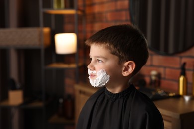 Photo of Little boy with shaving foam on his face in barbershop, space for text
