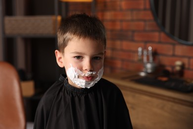 Photo of Little boy with shaving foam on his face in barbershop, space for text