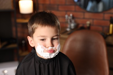 Photo of Little boy with shaving foam on his face in barbershop