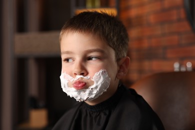 Photo of Little boy with shaving foam on his face in barbershop
