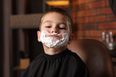 Photo of Little boy with shaving foam on his face in barbershop