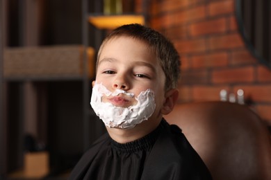 Photo of Little boy with shaving foam on his face in barbershop