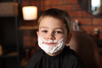 Photo of Little boy with shaving foam on his face in barbershop