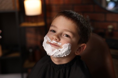 Photo of Little boy with shaving foam on his face in barbershop