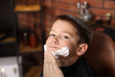 Photo of Professional barber applying shaving foam onto boy's face in barbershop, closeup. Space for text