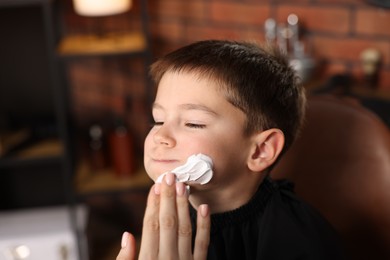 Photo of Professional barber applying shaving foam onto boy's face in barbershop, closeup. Space for text