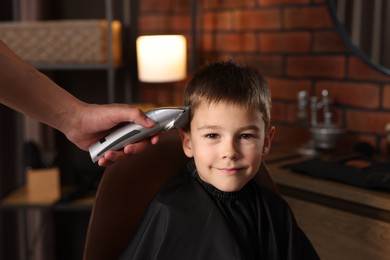 Photo of Professional barber working with little boy in barbershop, closeup