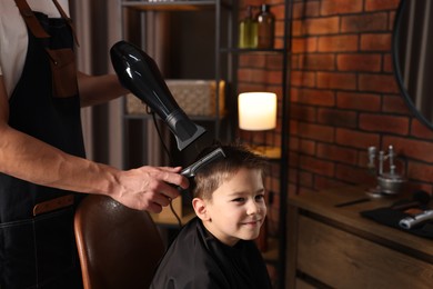 Photo of Professional barber blow drying boy's hair in barbershop, closeup