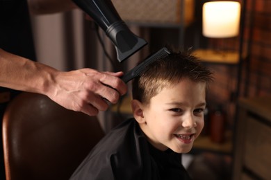 Photo of Professional barber blow drying boy's hair in barbershop, closeup