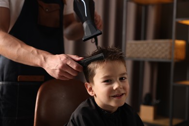 Photo of Professional barber blow drying boy's hair in barbershop, closeup