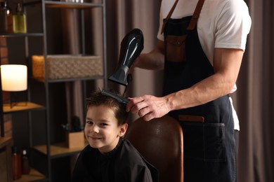 Photo of Professional barber blow drying boy's hair in barbershop, closeup