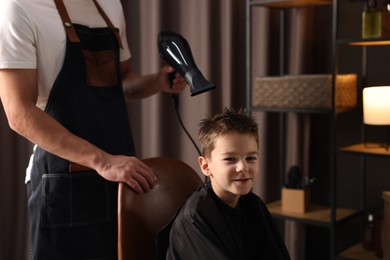 Photo of Professional barber blow drying boy's hair in barbershop, closeup