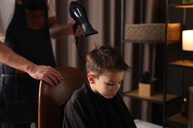 Photo of Professional barber blow drying boy's hair in barbershop, closeup
